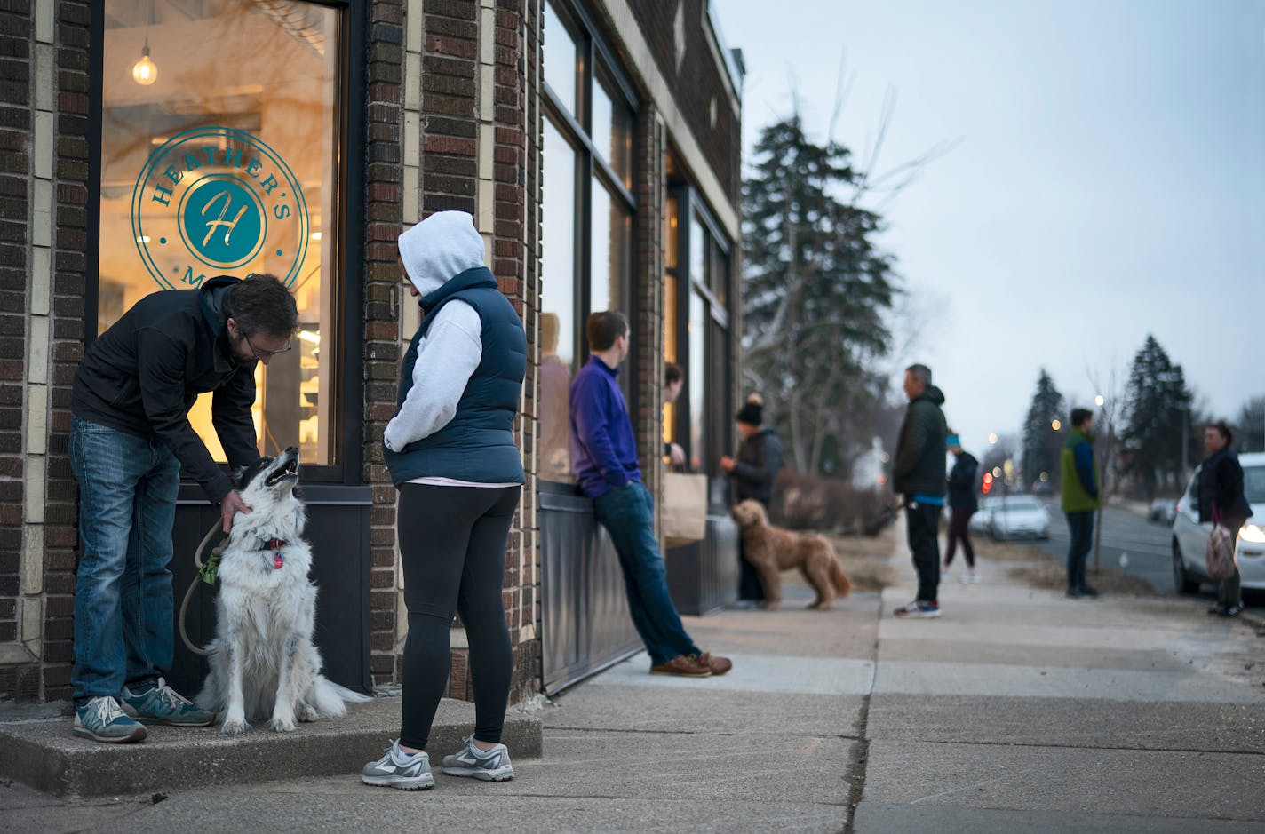 Tyson and Amanda Heinz gave some attention to their dog, Lola, while they waited with other customers for takeout orders outside Heather's on Chicago Ave. S. in south Minneapolis Wednesday night. The sliding glass walk-up window at rear, intended for summer ice cream orders, has proven very handy since the takeout only policy has been initiated in Minneapolis due to the coronavirus outbreak.