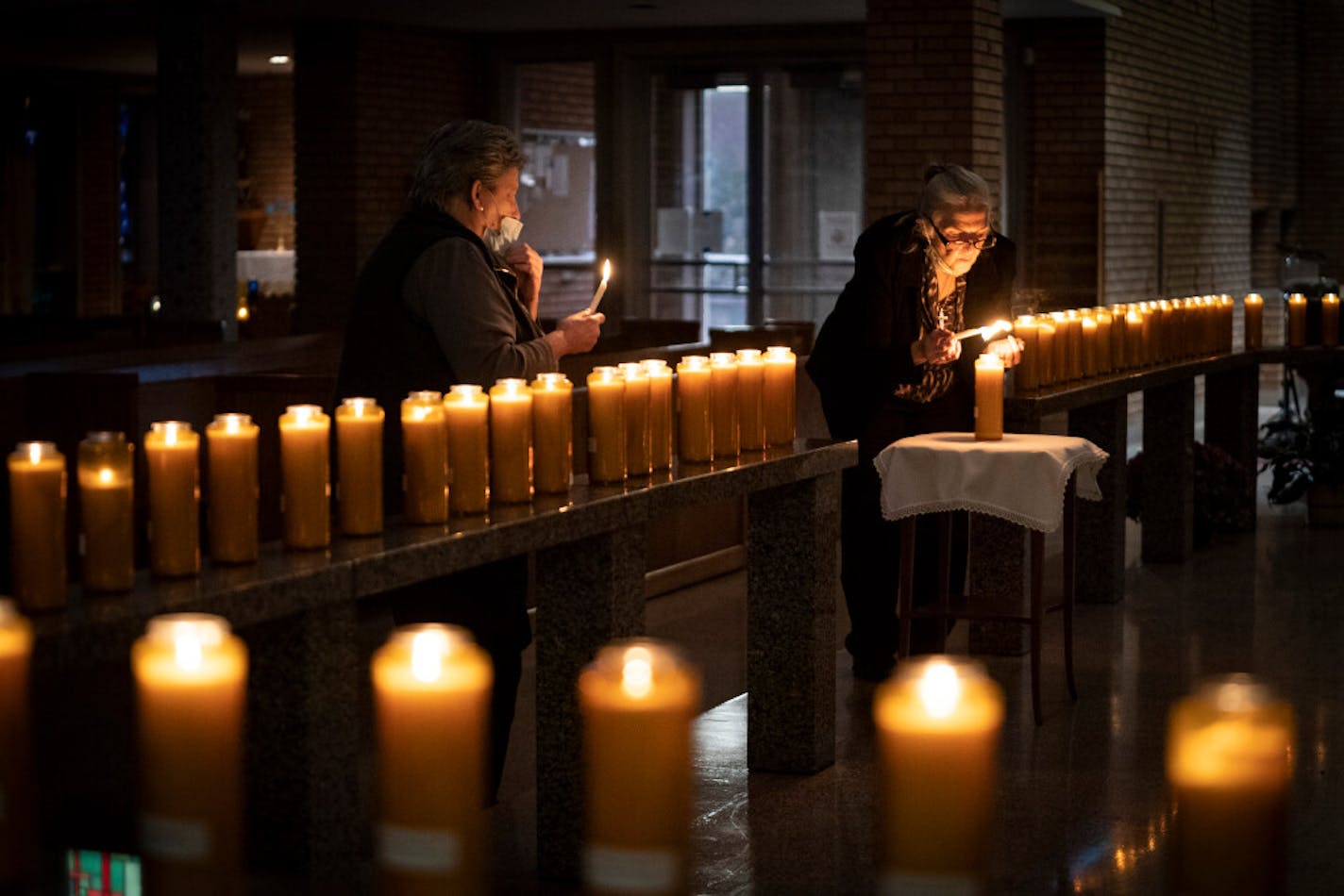 Left to right, Jodi Sandlin lit some of the more than 100 candles for loved ones of parish members who have died as Cece Ryan lit a candle in remembrance of those who died of COVID-19 during an All Souls' Day service at St. Bridget Catholic Church in Minneapolis on Monday, Nov, 2, 2020.