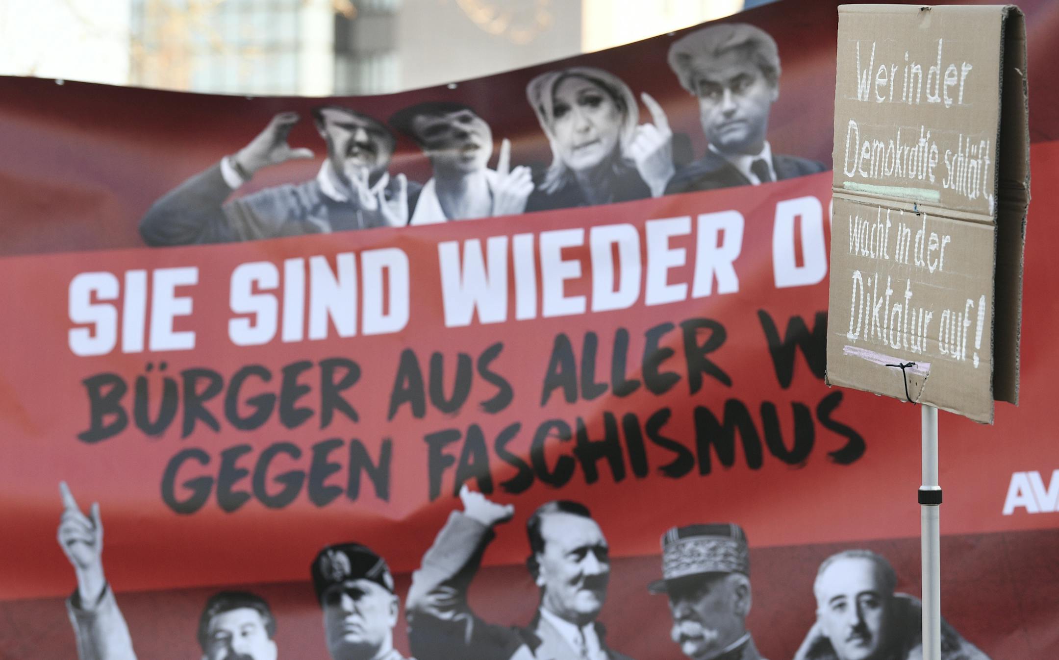 Demonstrators hold up a banner written with 'They're back!' Citizens from around the world against facism!' showing photos of Nationalist politicians on top an dictators from the 20th century at the bottom as the protest against a meeting of the ENF in Koblenz, Germany, Saturday, Jan. 21, 2017. The poster in front reads 'Who sleeps in democracy wakes up in a dictatorship'. (Boris Roessler/dpa via AP)
