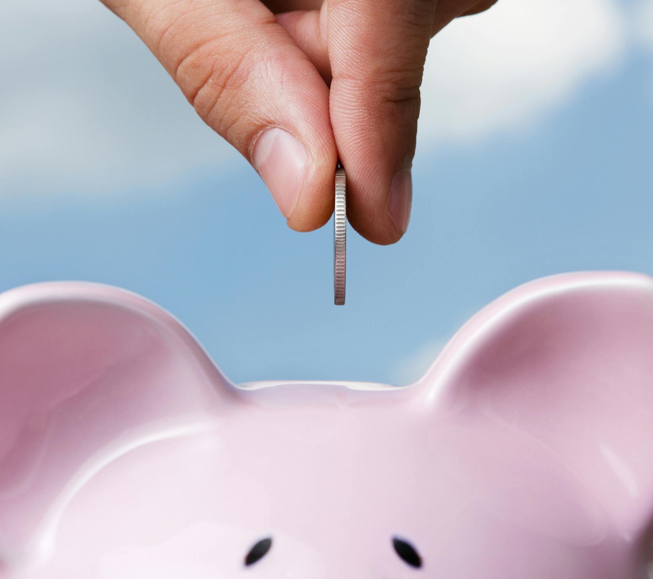 Male hand putting a coin into piggy bank