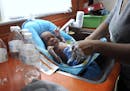 In this Thursday, Jan. 28, 2016 photo, Porshe Loyd, uses bottled water to wash her three-week-old son, LeAndrew, in a baby bather in the kitchen sink 
