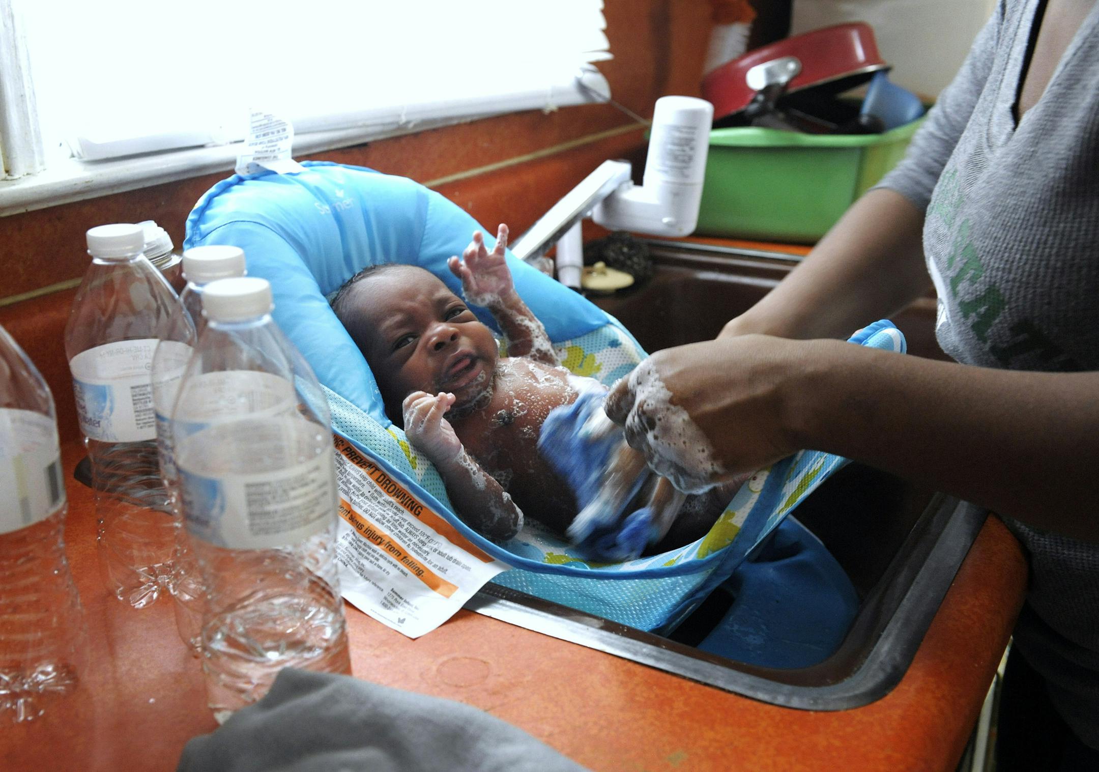 In this Thursday, Jan. 28, 2016 photo, Porshe Loyd, uses bottled water to wash her three-week-old son, LeAndrew, in a baby bather in the kitchen sink at their home in Flint, Mich. At home she has cases of bottled water that she bought or received from the Flint Fire Department or Michigan State Police troopers stored along a wall. Improperly treated water leached lead from pipes into drinking water after Flint switched from Detroit's water system to the Flint River in 2014 to save money while un