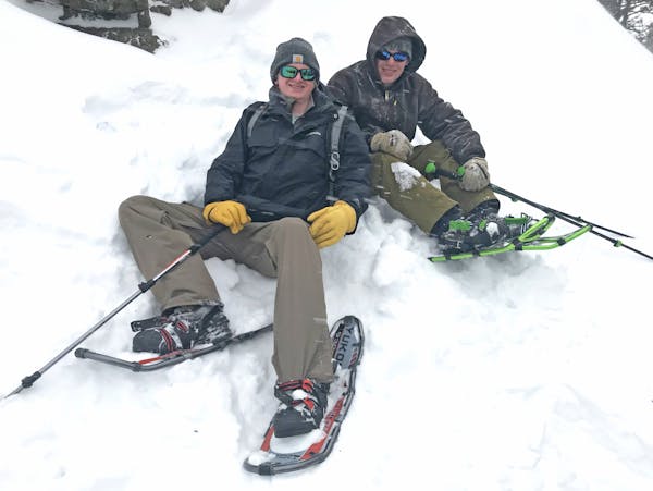 Cole Anderson, left, and Max Kelly relax in snow after hiking on snowshoes to a rocky peak in the Bridger Mountains of Montana.