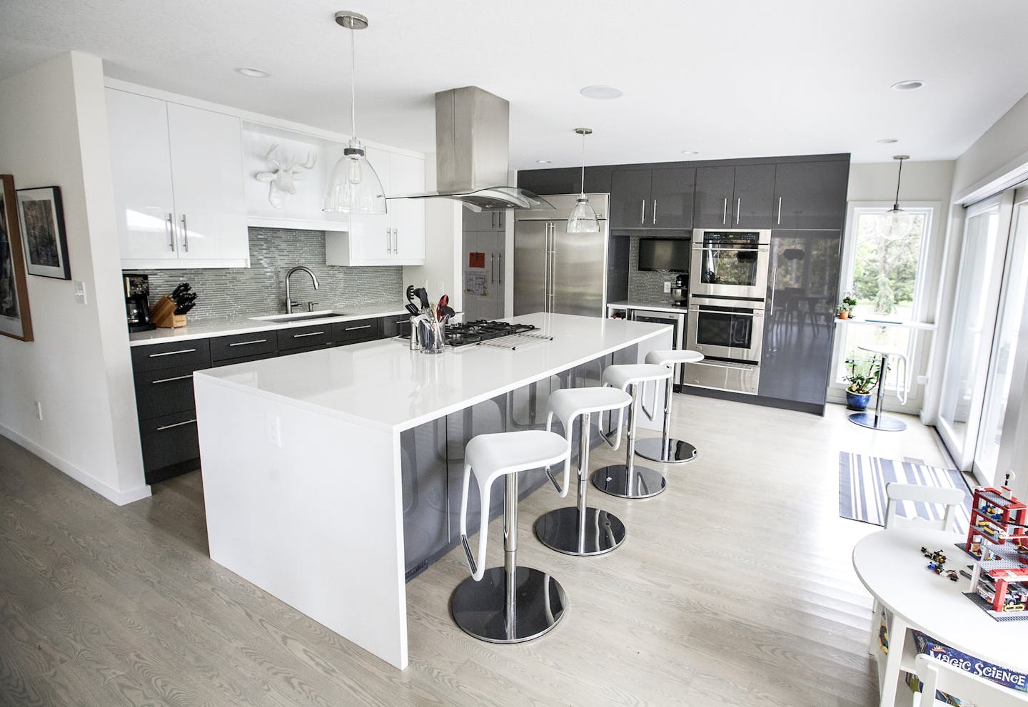 Gray-washed oak floors warm up the reflective charcoal and white surfaces. The kitchen's sliding door opens to a spacious outdoor room on the large wooded lot.