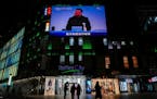 Residents walk by a screen showing Chinese President Xi Jinping wearing a face mask attending the closing ceremony.