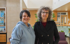 Two women smile and stand beside each other in a campus building.