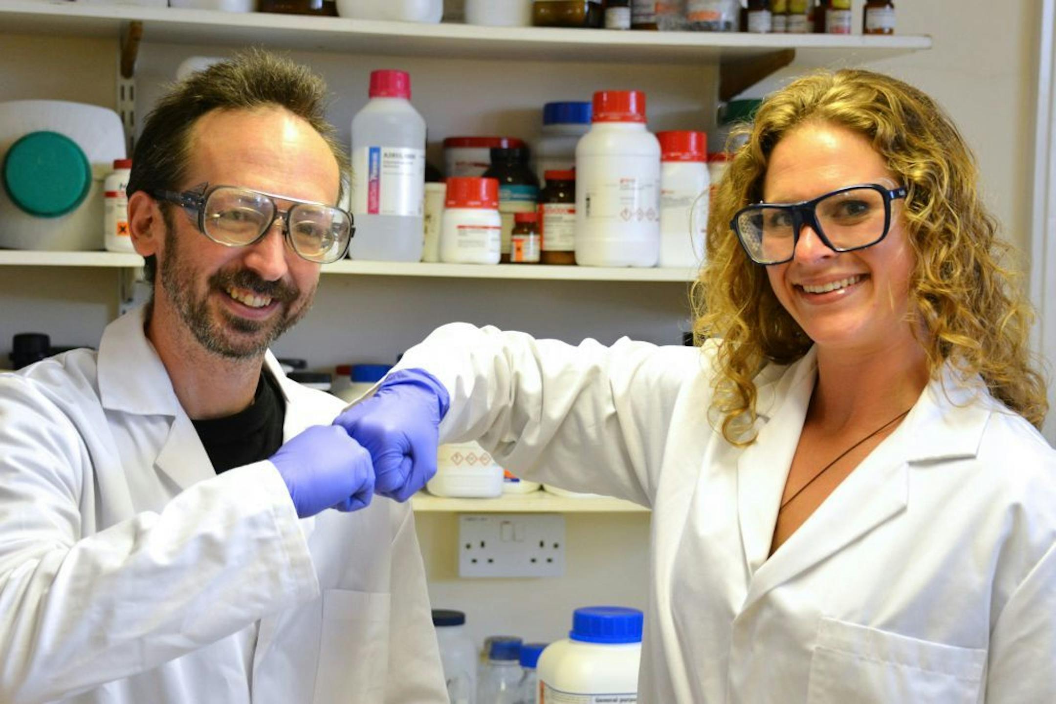 In this undated photo provided by Prifysgol Aberystwyth University researchers David Whitworth, left, and Sara Mela, pose for photo in the lab at Prifysgol Aberystwyth University in Aberystwyth, Wales. According to results published online Monday, July 28, 2014, in the American Journal of Infection Control the researchers found that the knocking of knuckles, fist bump, spreads only one-twentieth the amount of bacteria that a handshake does.