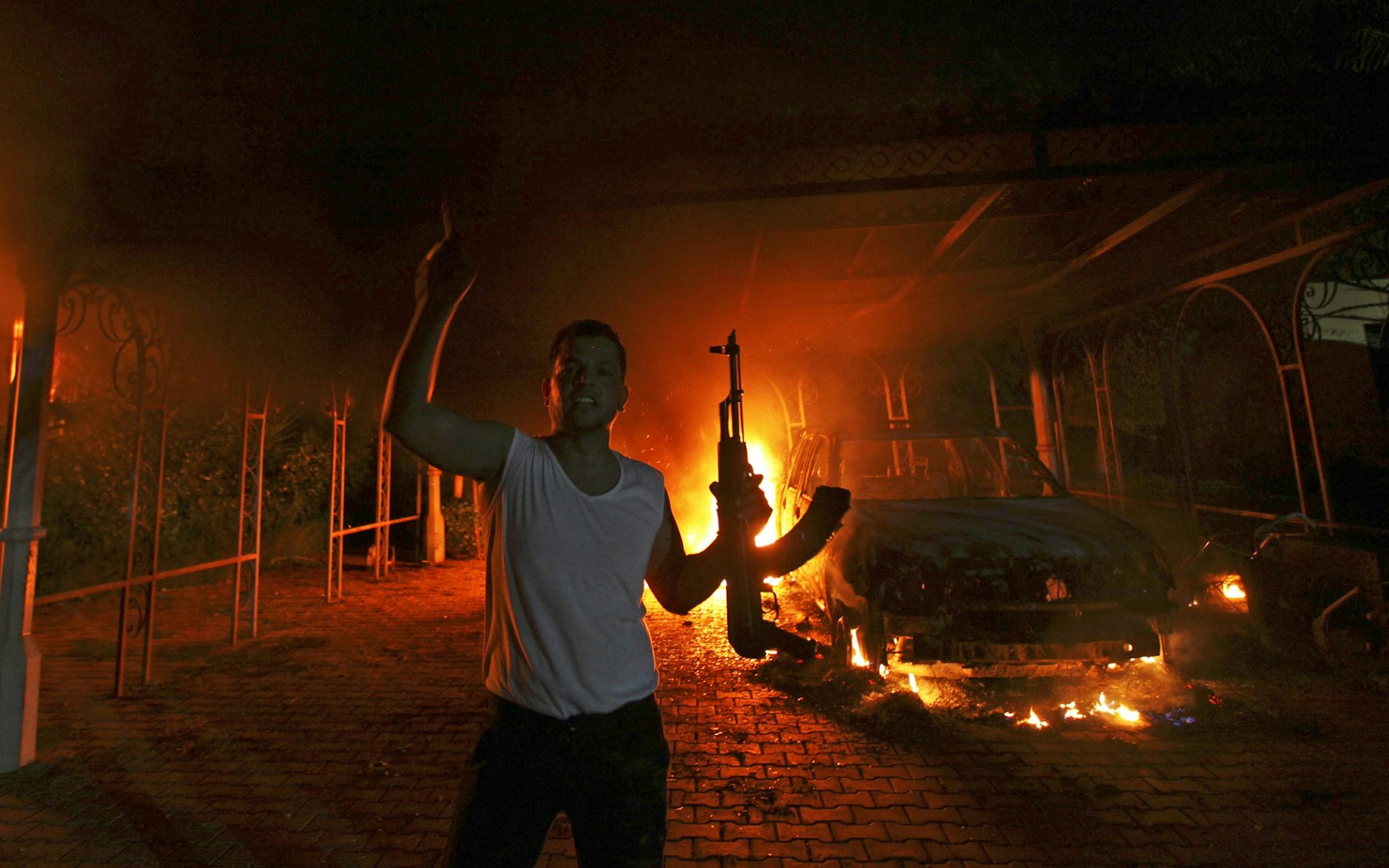 A protester reacts as the U.S. Consulate in Benghazi is seen in flames during a protest by an armed group said to have been protesting a film being produced in the United States September 11, 2012. An American staff member of the U.S. consulate in the eastern Libyan city of Benghazi has died following fierce clashes at the compound, Libyan security sources said on Wednesday. Armed gunmen attacked the compound on Tuesday evening, clashing with Libyan security forces before the latter withdrew as