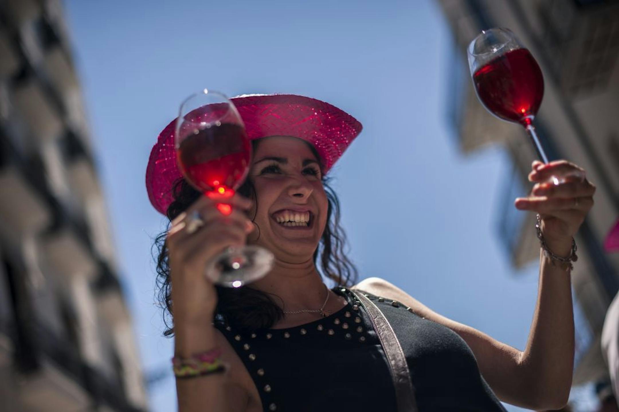 A woman smiles while she holds two glasses of rose wine during a tasting on the street to promote this Spanish wine on a sunny spring day, in Pamplona northern Spain, Saturday, May 17, 2014. Spanish rose wine is a typical wine of this zone of Spain.