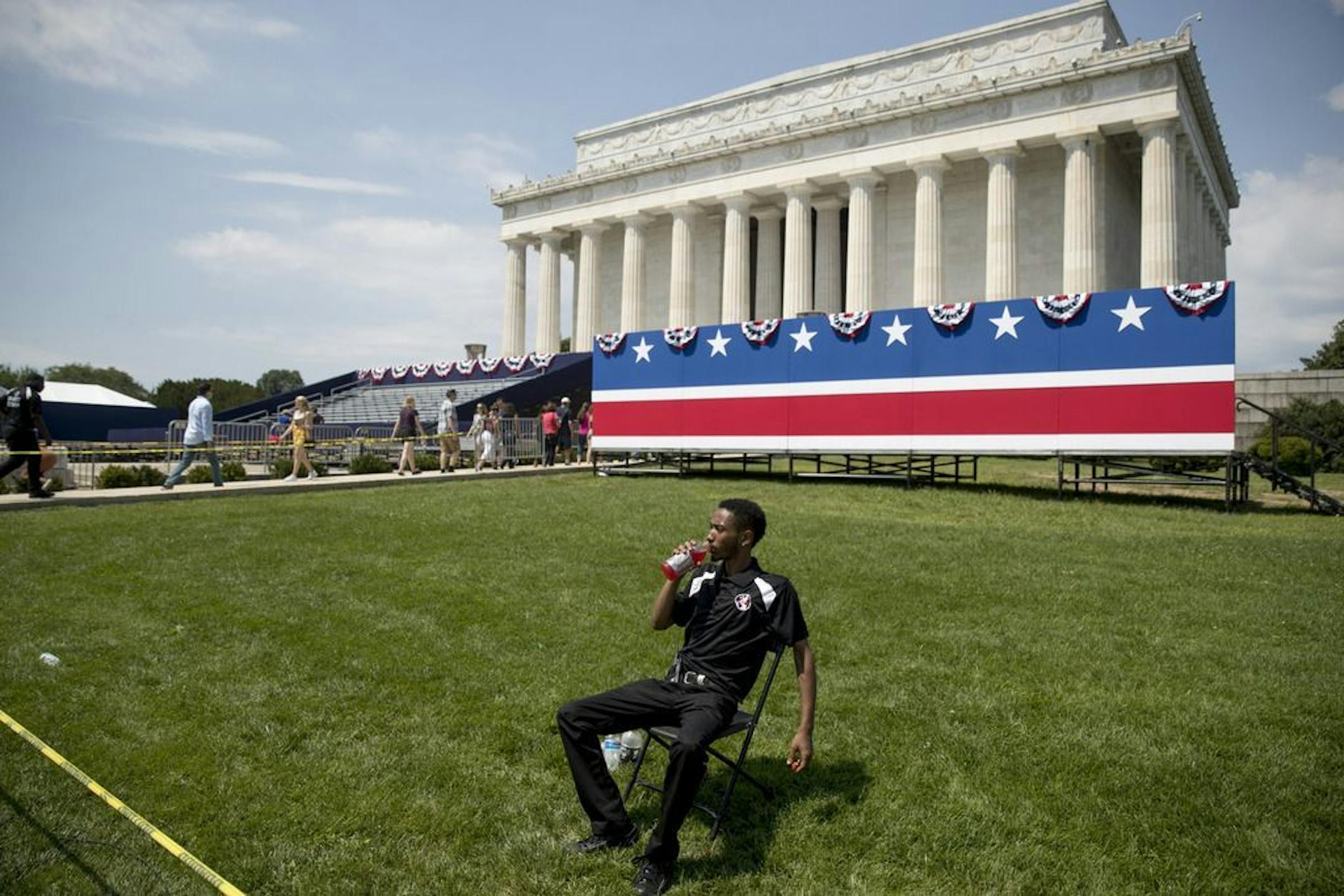 An event staff member sits in the grass as workers set up for President Donald Trump's 'Salute to America' event honoring service branches on Independence Day at the Lincoln Memorial, Tuesday, July 2, 2019, in Washington. President Donald Trump is promising military tanks along with "Incredible Flyovers & biggest ever Fireworks!" for the Fourth of July.
