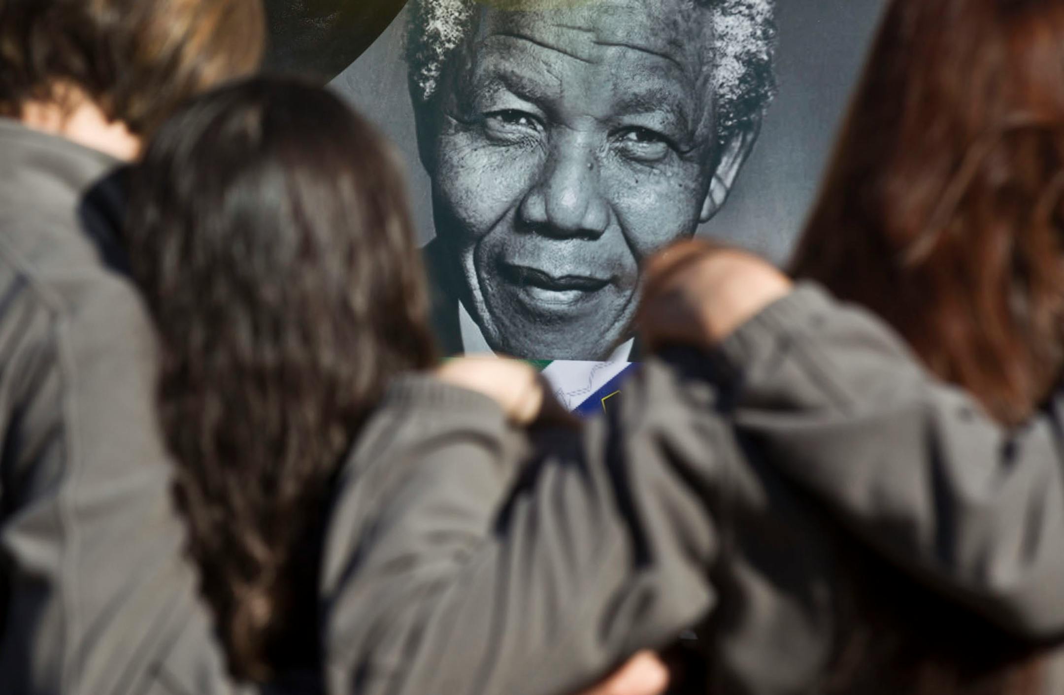 Members of the Toronto Children's Chorus choral group from Toronto, Ontario, Canada, who are on a tour taking part in the Ihlombe South African Choral Festival, hug each other as they observe some of the get-well messages and flowers, after singing outside the Mediclinic Heart Hospital where former South African President Nelson Mandela is being treated in Pretoria, South Africa Saturday, July 13, 2013.