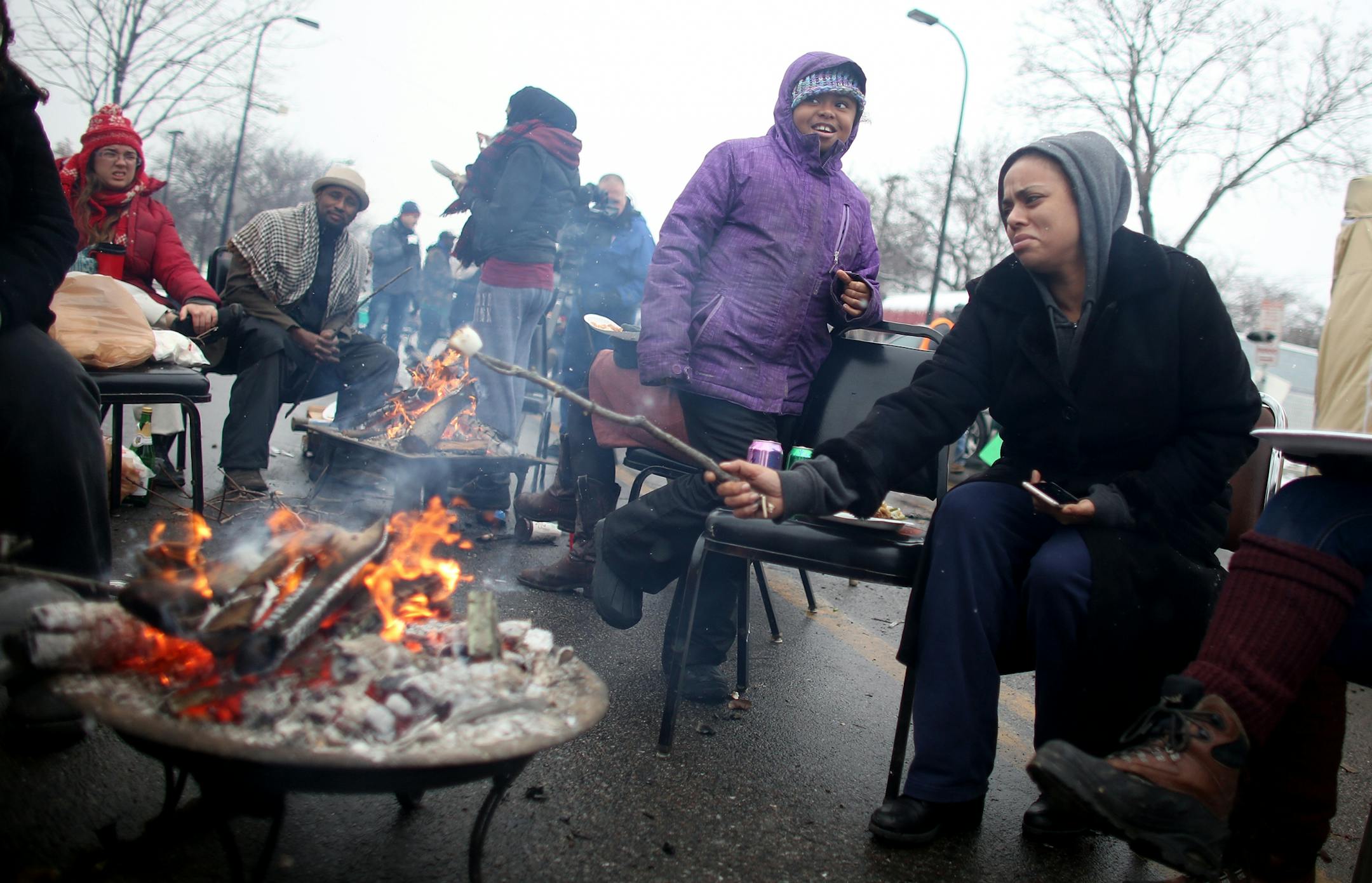 Bronwen Weissbrodt, with smoke in her eye, tried to roast a marshmallow for Aaliyah Proctor, 7, during BlackGiving event in front of the Minneapolis Fourth Precinct.