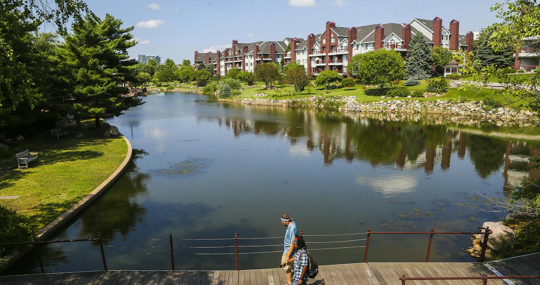 Avery Rowell, far bottom, and Rob Hoagberg, above, converse while walking over a brigge connectnig the park over the man-made pond. ] Timothy Nwachukwu &#x2022; timothy.nwachukwu@startribune.com Visitors enjoy a warm Minnesota summer afternoon at Centennial Lakes Park on Wednesday, July 20, 2016 in Edina. The development was recognized as one the the Great Places of 2014 by the Sensible Land Use Coalition. ORG XMIT: MIN1607202105230750