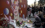 People lay flowers next to a mural of British singer David Bowie by artist Jimmy C in Brixton, south London, Monday, Jan. 11, 2016. Bowie, the other-w
