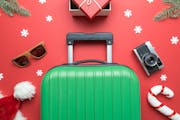 Christmas holiday minimal creative composition made of suitcase, gift box, sunglasses,Santa hat, candy cane, retro photo camera, fir branches and snow