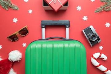 Christmas holiday minimal creative composition made of suitcase, gift box, sunglasses,Santa hat, candy cane, retro photo camera, fir branches and snow