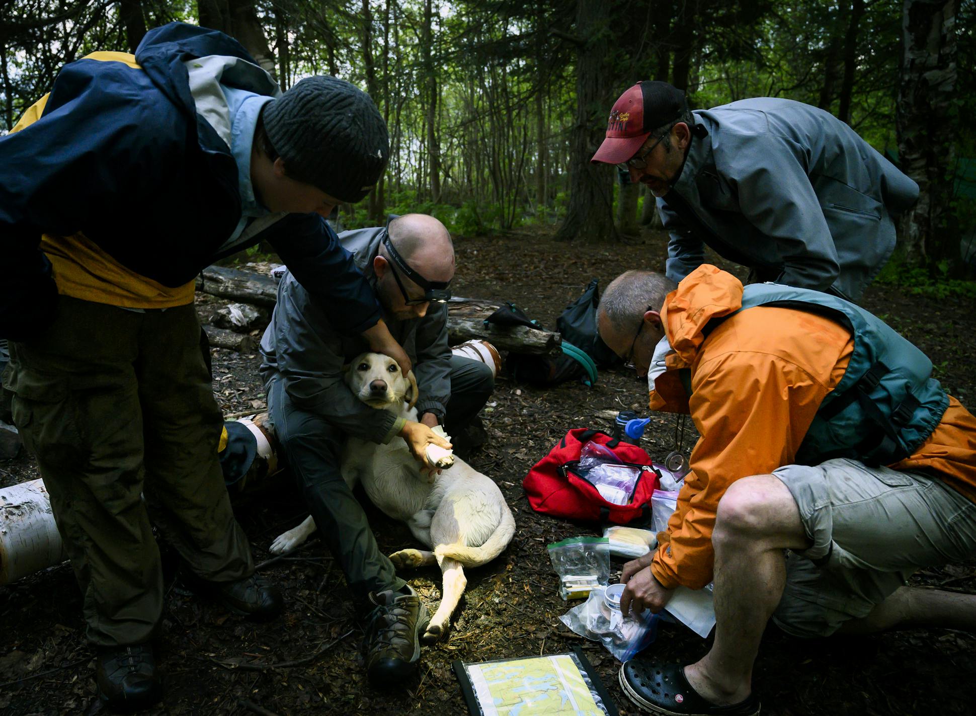 Tony Jones held his dog, Crosby, as Brad Shannon, lower right, cleaned a gash and bandaged it. Crosby suffered the cut on a boulder field.