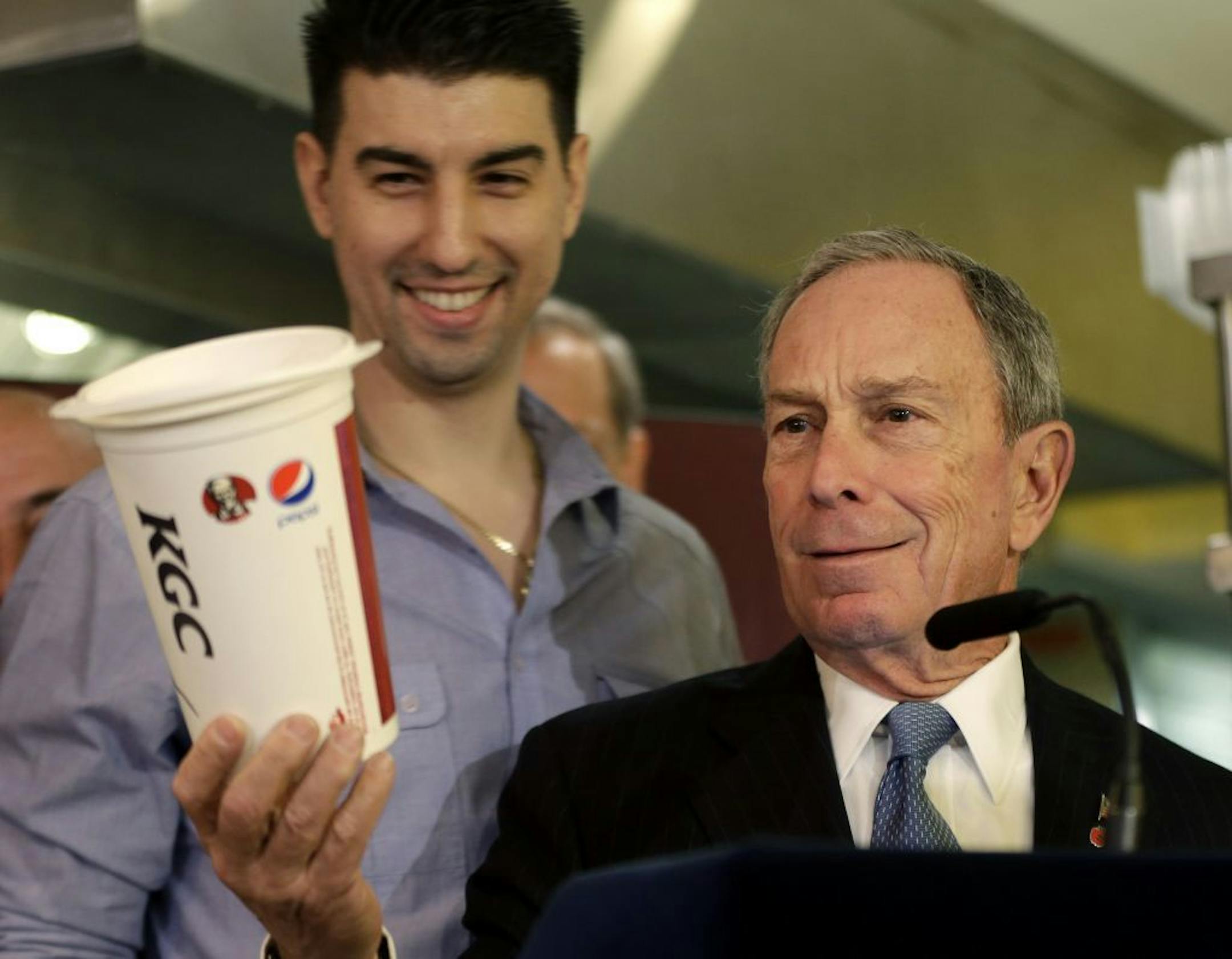 New York City Mayor Michael Bloomberg looks at a 64oz cup, as Lucky's Cafe owner Greg Anagnostopoulos, left, stands behind him, during a news conference at the cafe in New York, Tuesday, March 12, 2013.