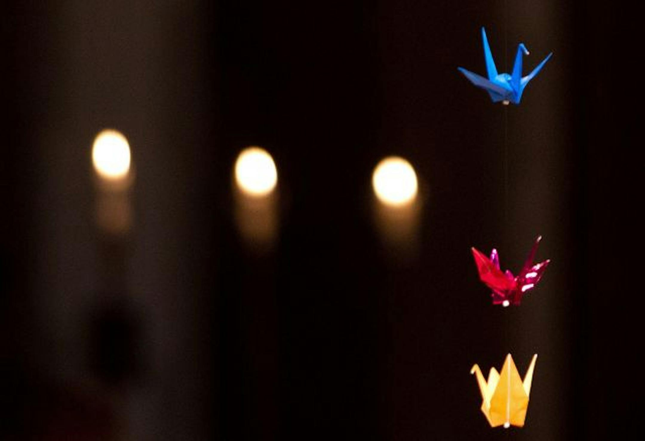 Paper cranes hang as candles burn during a prayer service for the people of Japan.