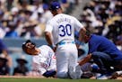 The Dodgers' Mookie Betts, left, writhes on the ground after being hit by a pitch in the left hand as manager Dave Roberts and a trainer tend to him S
