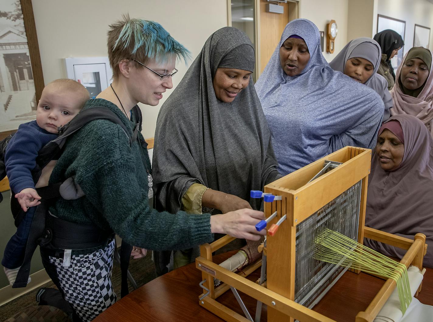 After receiving a Halal meal from the St. Peter Food Club grocery and deli, Caitlin Heyer, with her son Arthur, showed East African women how to use a desk loom to weave a scarf at the St. Peter Senior Center, Thursday, November 14, 2019. The women are taking part in a newly founded program that provides East African elders living in and around St. Peter with a culturally appropriate meal and connects immigrants and refugees with community services. ] ELIZABETH FLORES &#x2022; liz.flores@startri