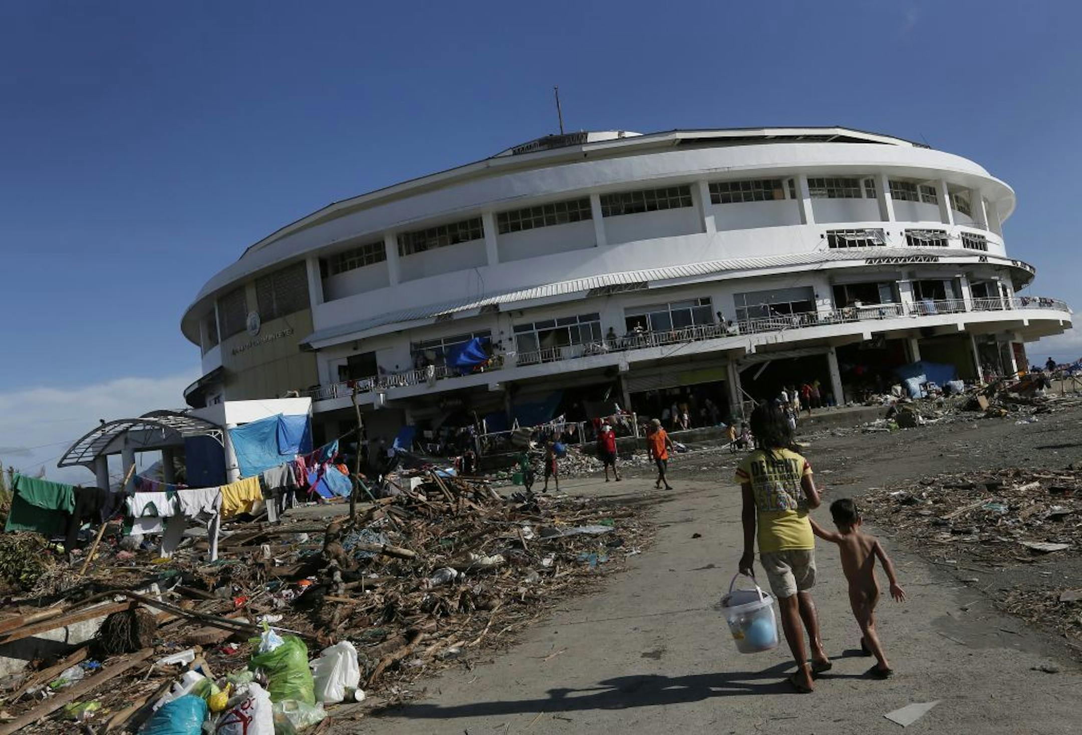 A young girl walks her brother to the Tacloban City Convention Center known as the Astrodome Thursday, Nov. 14, 2013, where hundreds of displaced typhoon survivors have set up makeshift shelters.