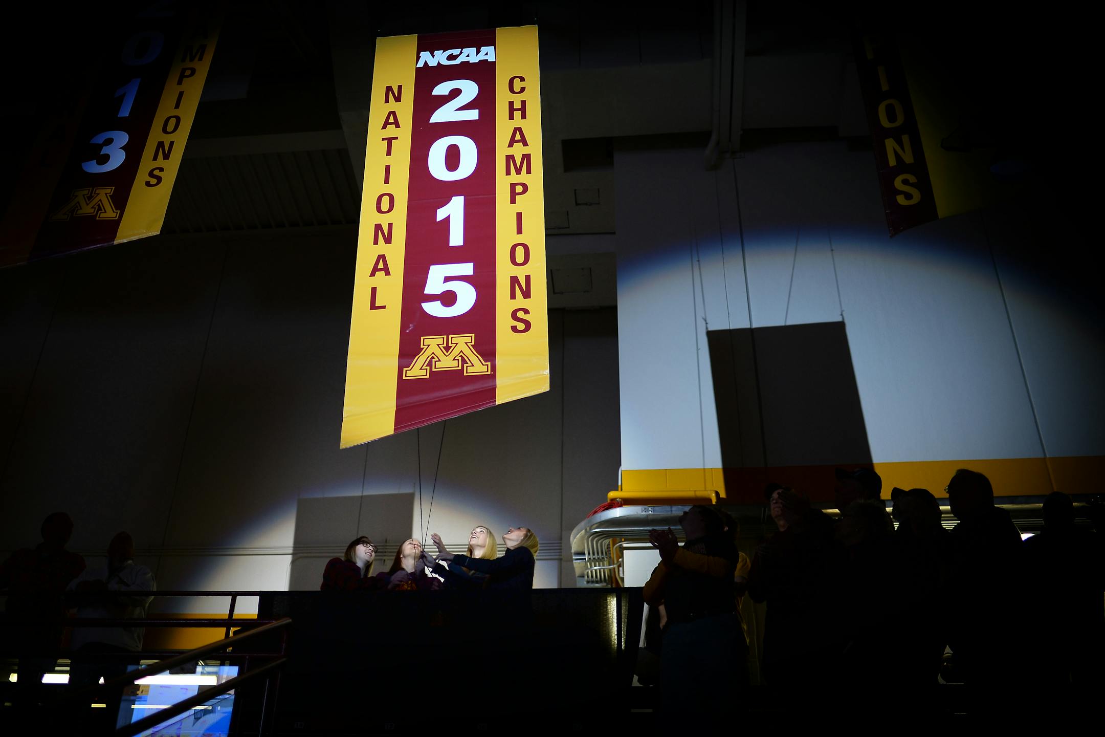 Members of the 2015 NCAA champion Minnesota hockey team including, from left, Shyler Sletta, Meghan Lorence, Rachael Bona and Rachel Ramsey, raise the championship banner before the team's game against St. Cloud State on Friday, Oct. 9, 2015, in Minneapolis.