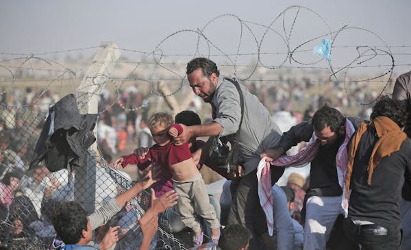 FILE - A Sunday, June 14, 2015 file photo of a Syrian refugee carrying a baby over the broken border fence into Turkey after breaking the border fence