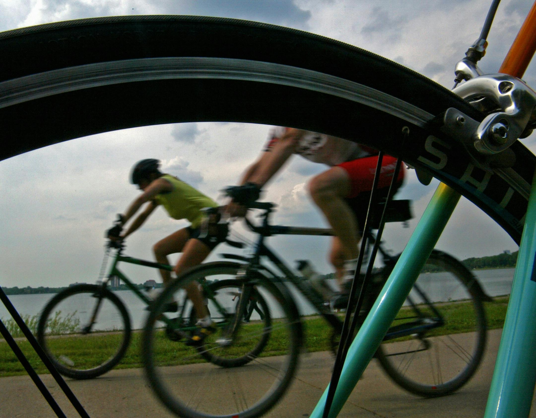 star tribune staff tom sweeney
Minneapolis, Mn 6/02/2005 a pair of cyclists, one riding a mountain bike, the other a 'commuter' framed through the wheel of a road racing bike as they ride the path at lake calhoun