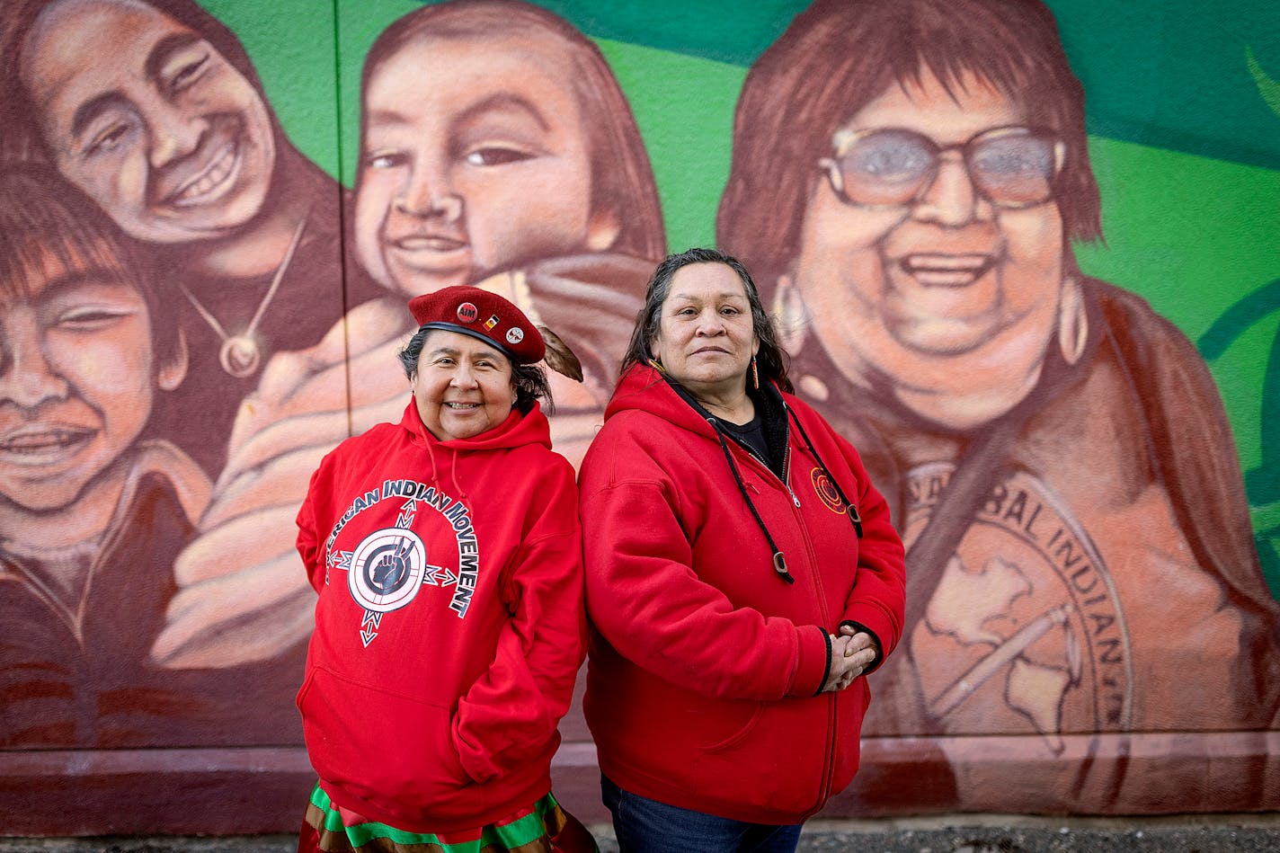 Local American Indian Movement directors Lisa Bellanger, left, Jackie Nadeau, right, stand in front of a mural, in Minneapolis, Minn., on Friday, Feb. 17, 2023. The mural is significant because it displays a painting of Pat Bellanger, known as "Grandmother AIM" and one of its original co-founders. Pat Bellanger Lisa's mother, participated in the Wounded Knee Occupation in 1973. She died in 2015. ] Elizabeth Flores • liz.flores@startribune.com