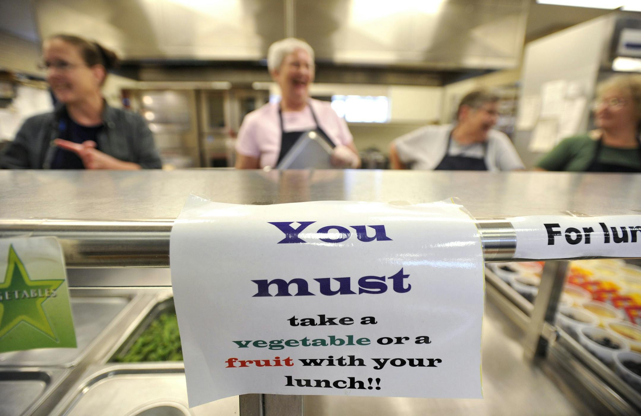 A sign is posted telling students to take a vegetable or fruit with their lunch at Wingate Elementary School, May 29, 2014 in Wingate, Pa. District officials had been working on more diverse fruit and veggie selections and heartier portions of those healthier choices long before the U.S. Department of Agriculture required it. They also had been working to switch to whole-grain breads. But the Bald Eagle Area School District has seen an increase in students packing lunches since implementing new