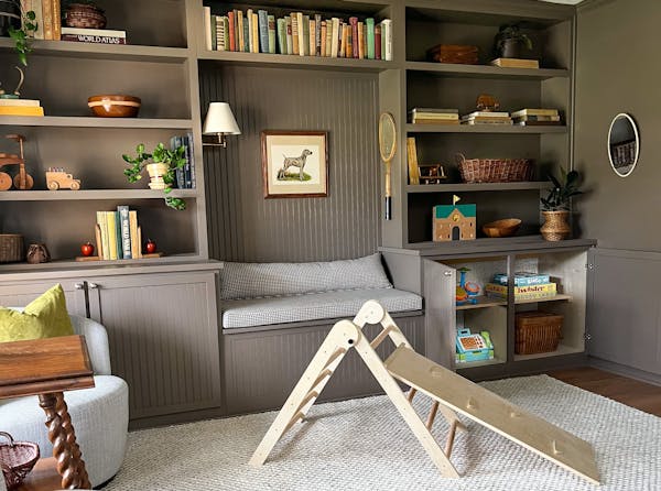 Dining room transformed into playroom with gray-brown built-in shelves with books and a reading nook, a rug over vinyl flooring and a small slide.