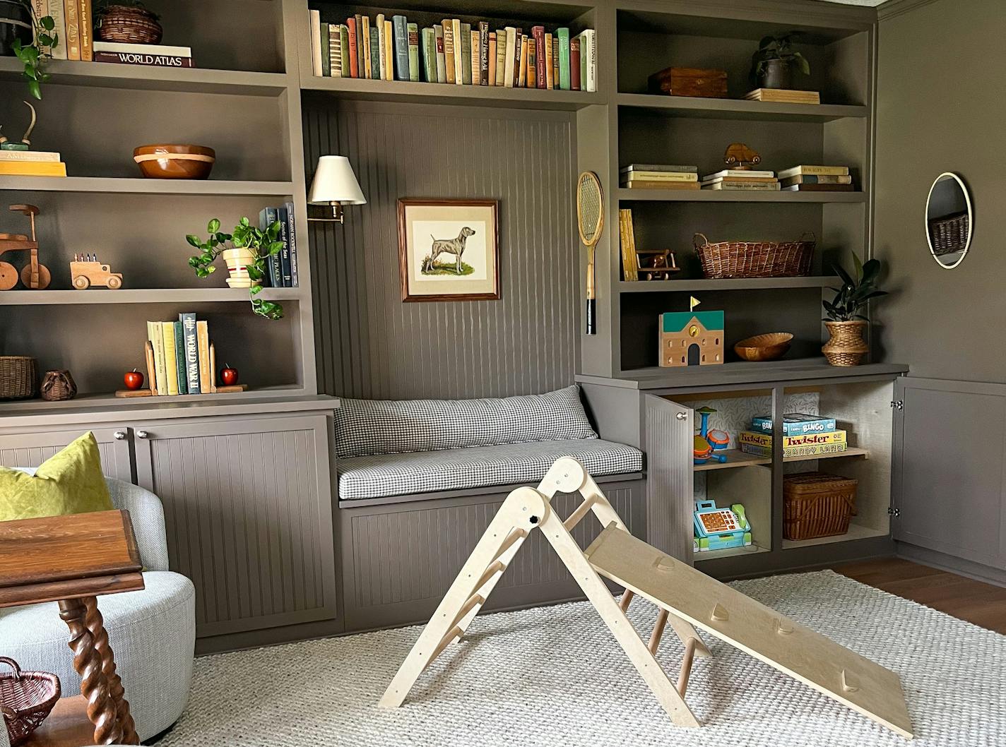 Dining room transformed into playroom with gray-brown built-in shelves with books and a reading nook, a rug over vinyl flooring and a small slide.