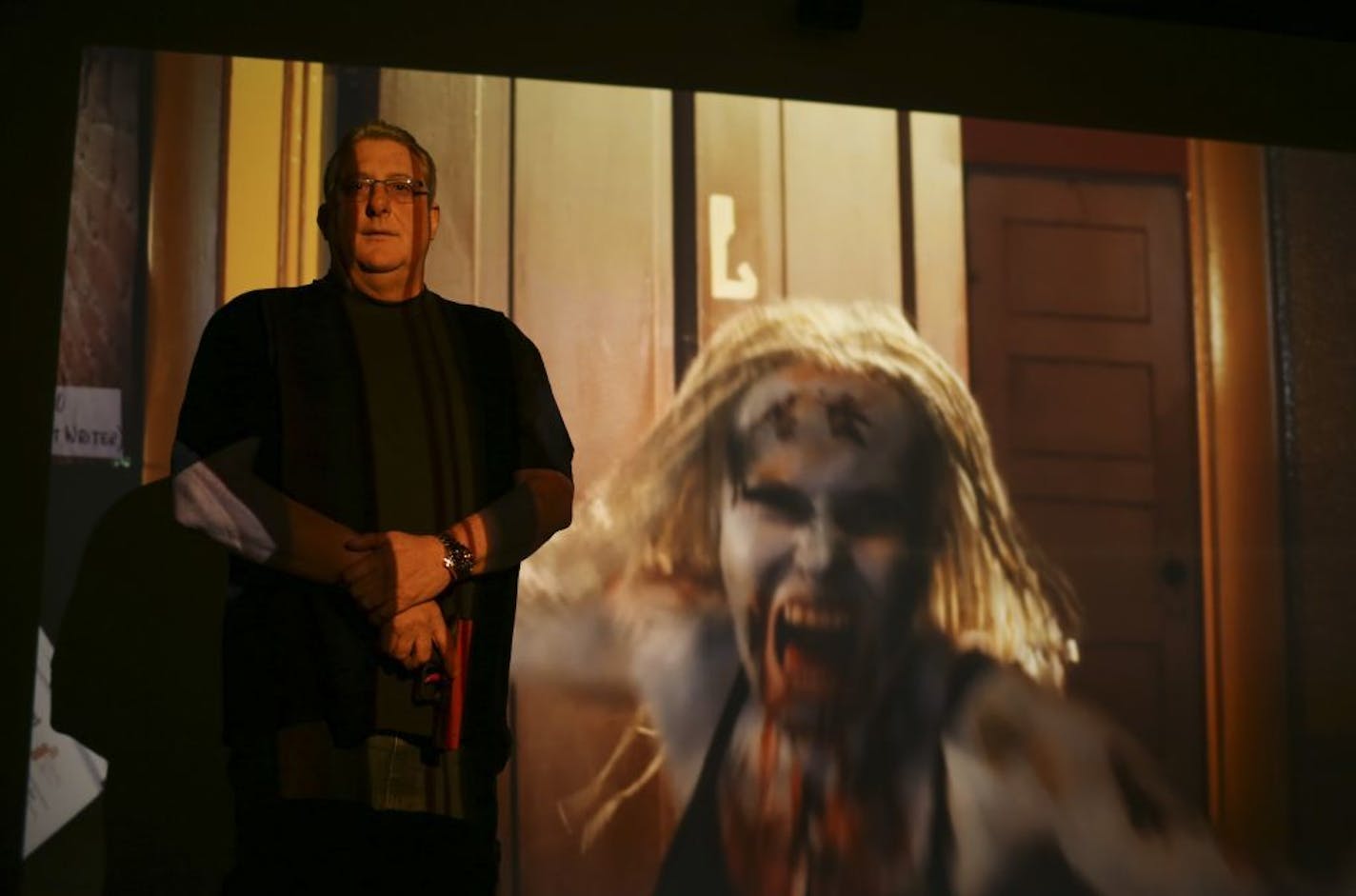 Chris Williamson, owner of the Osseo Gun Club & Pro Shop, in a room dedicated to firearms simulator training. The training scenario on the screen involves a zombie apocalypse.