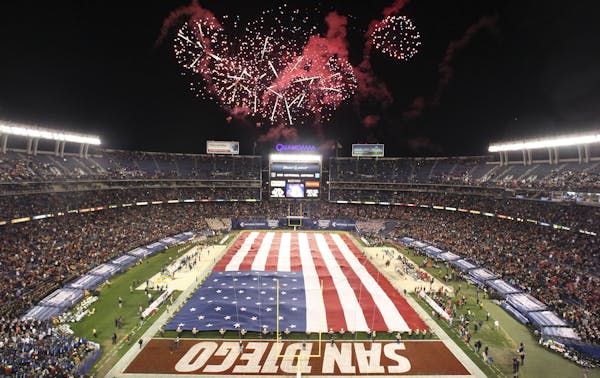 Fireworks explode as the national anthem plays while Marines hold a large U.S. flag during the opening ceremony for the National Funding Holiday Bowl 