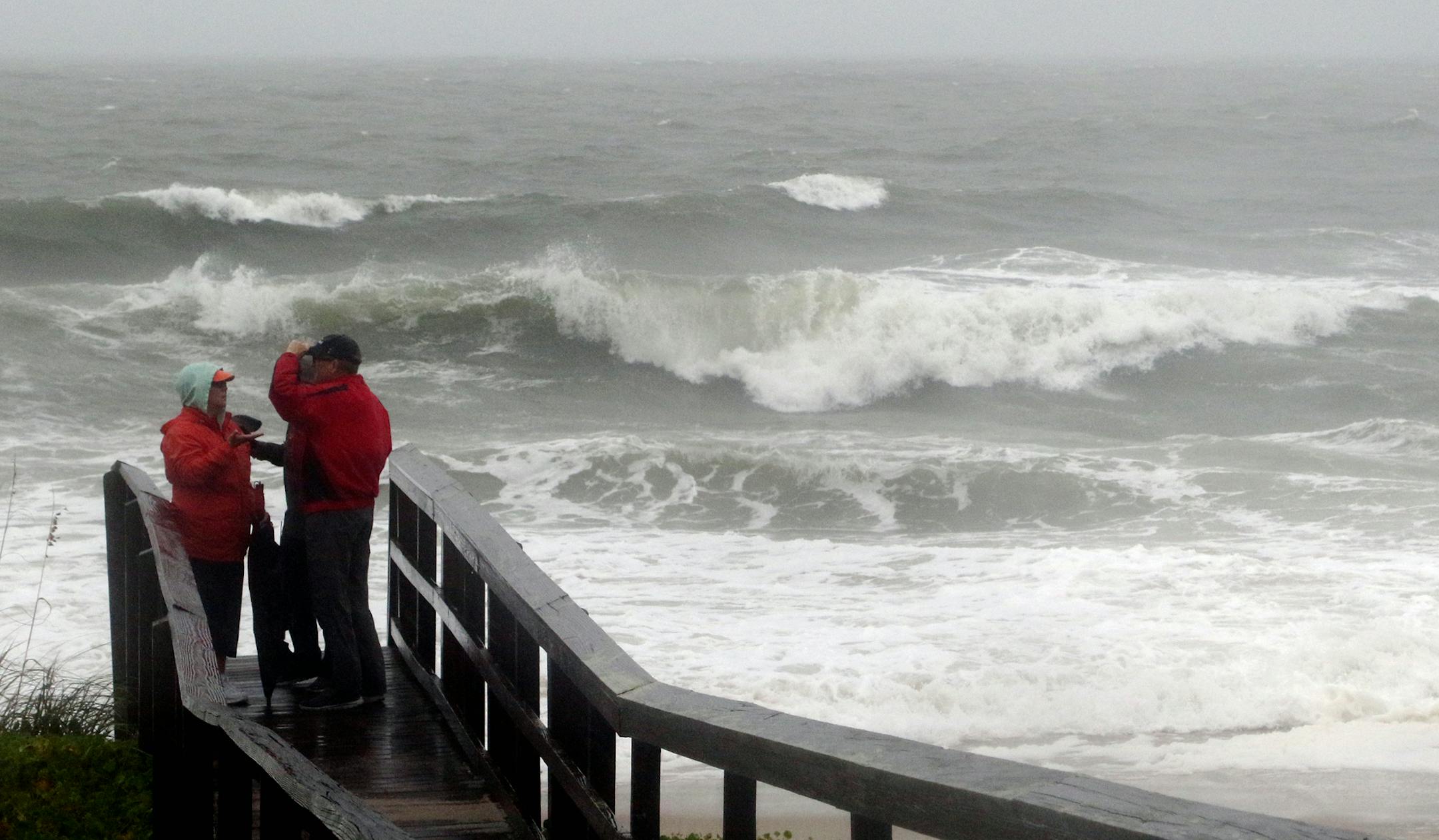 People watch the waves in a rainstorm at Atlantic Ocean at Carolina Beach, N. C., Friday, Oct. 2, 2015. Millions along the East Coast breathed a little easier Friday after forecasters said Hurricane Joaquin would probably veer out to sea instead of joining up with a drenching rainstorm that is bringing severe flooding to parts of the Atlantic Seaboard. (AP Photo/Harry Hamburg)