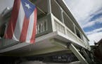 A Puerto Rican flag hangs from the porch of a home that collapsed on top of parked cars after an earthquake hit Guanica, Puerto Rico, Monday, Jan. 6, 