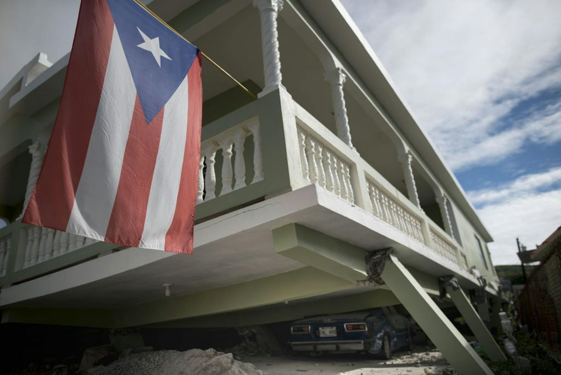 A Puerto Rican flag hangs from the porch of a home that collapsed on top of parked cars after an earthquake hit Guanica, Puerto Rico, Monday, Jan. 6, 2020. A 5.8-magnitude quake hit Puerto Rico before dawn Monday, unleashing small landslides, causing power outages and severely cracking some homes. There were no immediate reports of casualties.