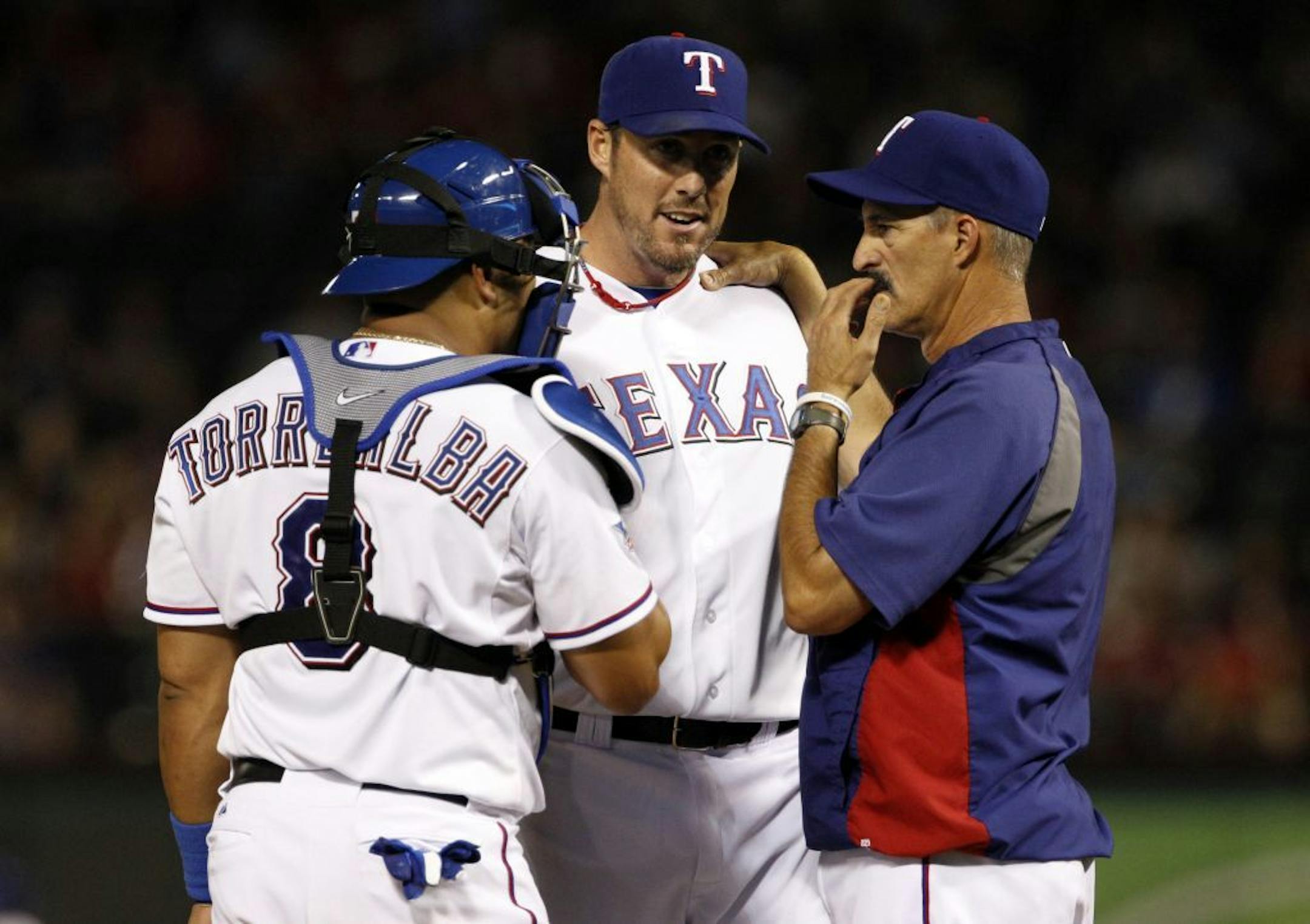 Texas Rangers catcher Yorvit Torrealba, left, and pitching coach Mike Maddux, right, visit closer Joe Nathan, center, in the ninth inning of a baseball game against the Seattle Mariners Wednesday, April 11, 2012, in Arlington, Texas. The Mariners won 4-3.