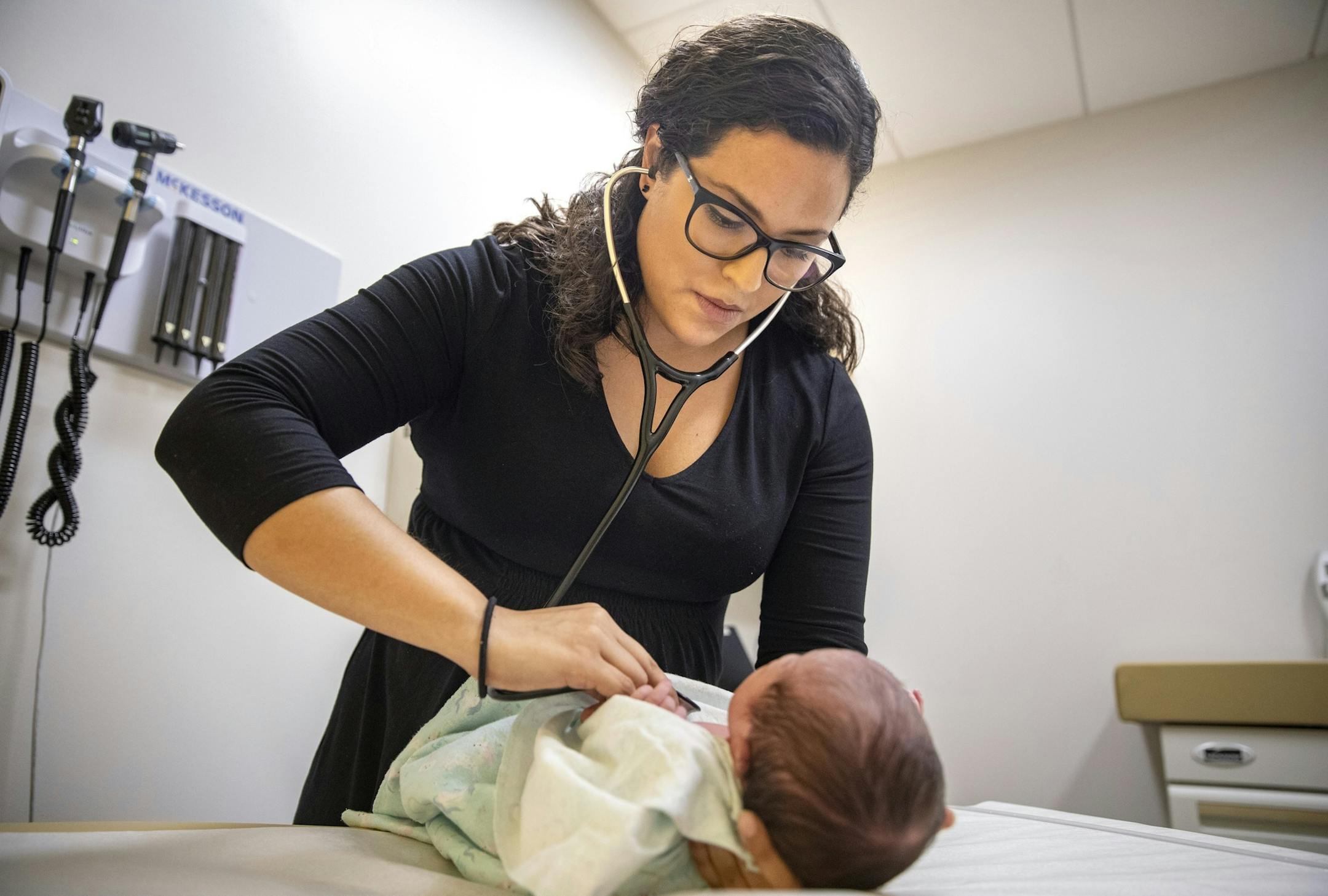 In this Tuesday, Aug. 13, 2019, photo, Dr. Jasmine Saavedra, a pediatrician at Esperanza Health Centers whose parents emigrated from Mexico in the 1980s, examines Alondra Marquez, a newborn baby in her clinic in Chicago. Doctors and public health experts warn of poor health outcomes and rising costs they say will come from sweeping changes that would deny green cards to many immigrants who use Medicaid, as well as food stamps and other forms of public assistance. Saavedra is convinced that if ne