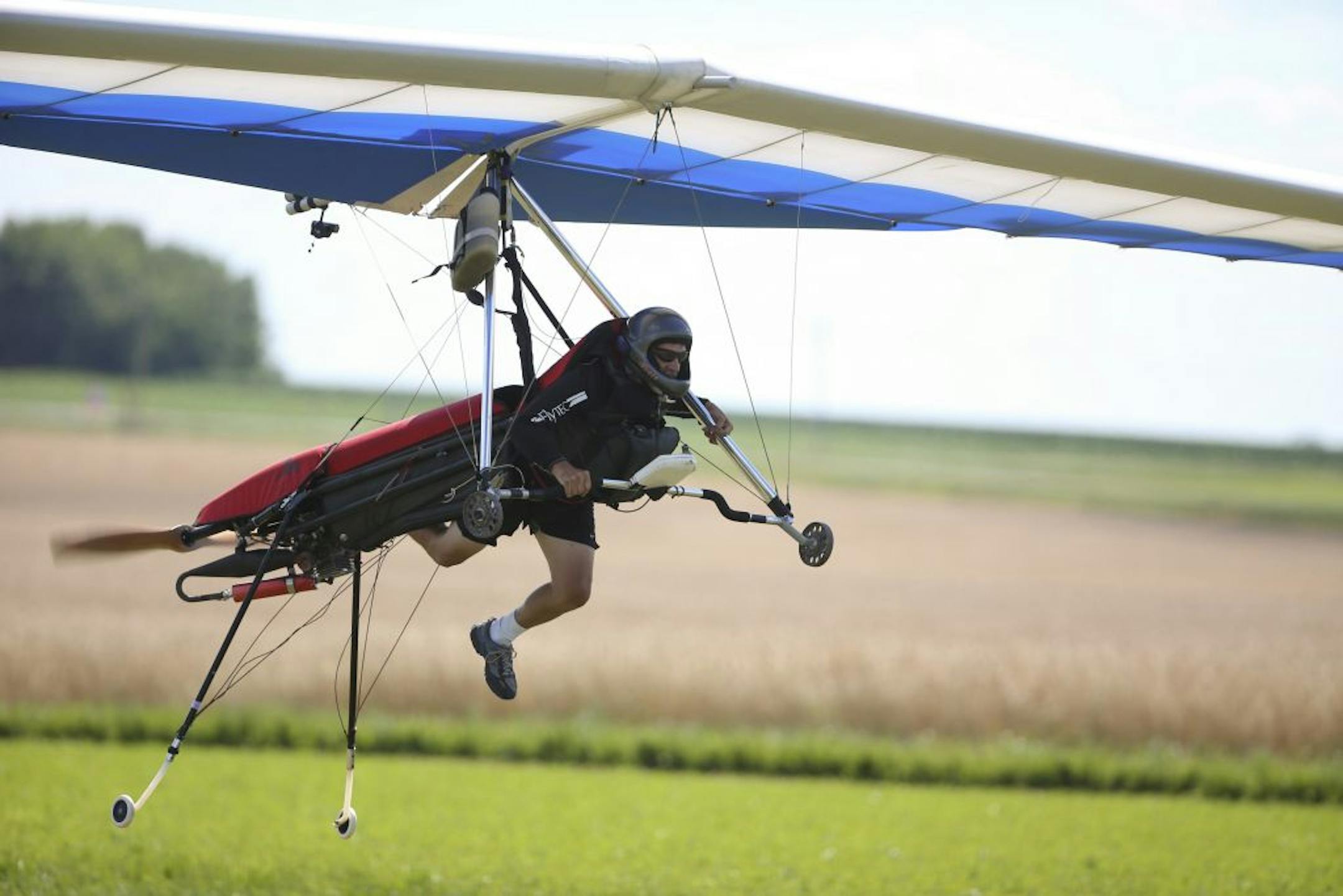 Gerry Uchytil, 59, of Hudson, Wisc. has been hang gliding for 40 years. Nowadays he uses a propeller assist to get up to altitude when launching from the ground, allowing him to take off from anywhere there's wind. A moment after liftoff from a tiny landing strip on a farmer's land in Rogers, Wisc. Monday afternoon, July 9, 2012, Gerry Uchytil began to tuck his legs into flying position on his motorized hang glider.