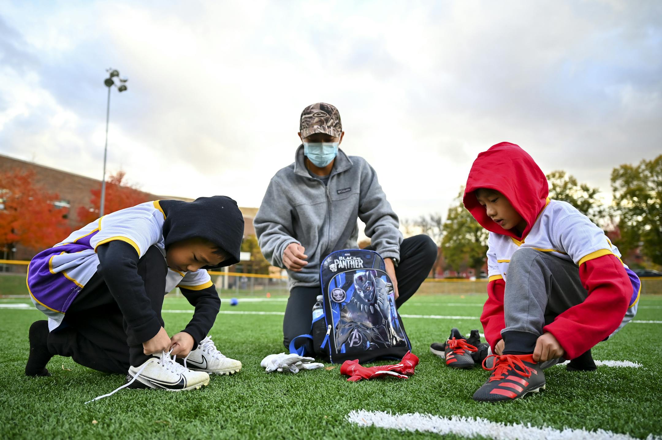 Davis Vue helped his sons Braedus, left, 6, and Memphis, 7, get ready for flag football practice Wednesday night. ] AARON LAVINSKY • aaron.lavinsky@startribune.com A story looking at how COVID-19 continues to impact youth sports. Between volunteer coaches having to add COVID protocols to their duties in some cities to others moving away from traditional soccer and football games to more of a skills camp setting, the virus didn't completely derail kids sports. But it sure changed what the kids, p