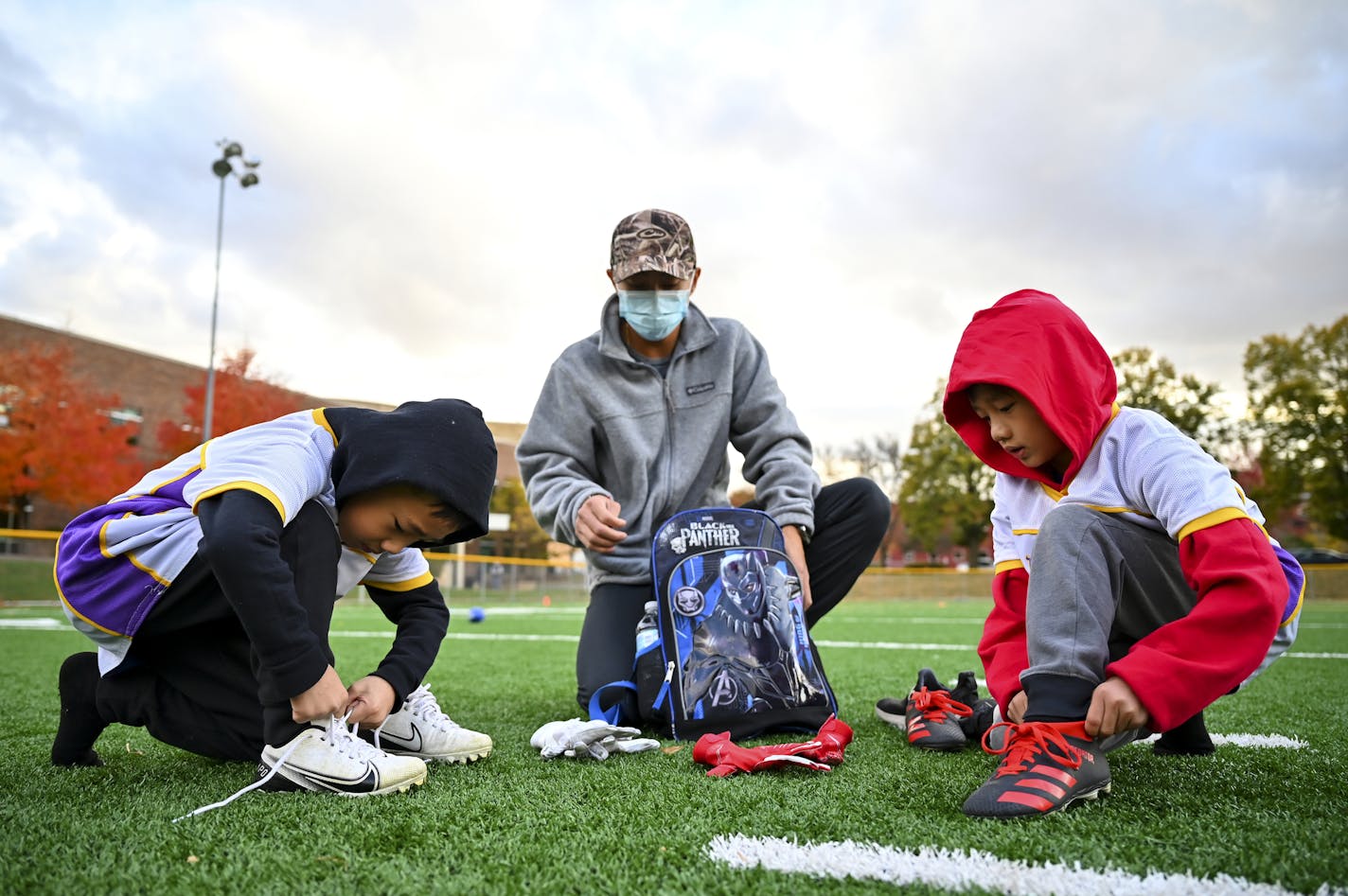 Davis Vue helped his sons Braedus, left, 6, and Memphis, 7, get ready for flag football practice Wednesday night. ] AARON LAVINSKY • aaron.lavinsky@startribune.com A story looking at how COVID-19 continues to impact youth sports. Between volunteer coaches having to add COVID protocols to their duties in some cities to others moving away from traditional soccer and football games to more of a skills camp setting, the virus didn't completely derail kids sports. But it sure changed what the kids, p