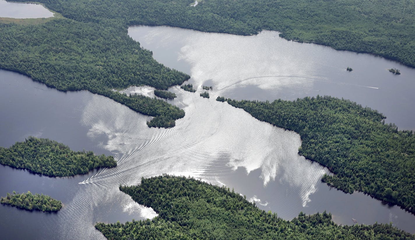 Motorized boats slice through reflections of clouds on Newfound Lake in the Boundary Waters Canoe Area Wilderness.