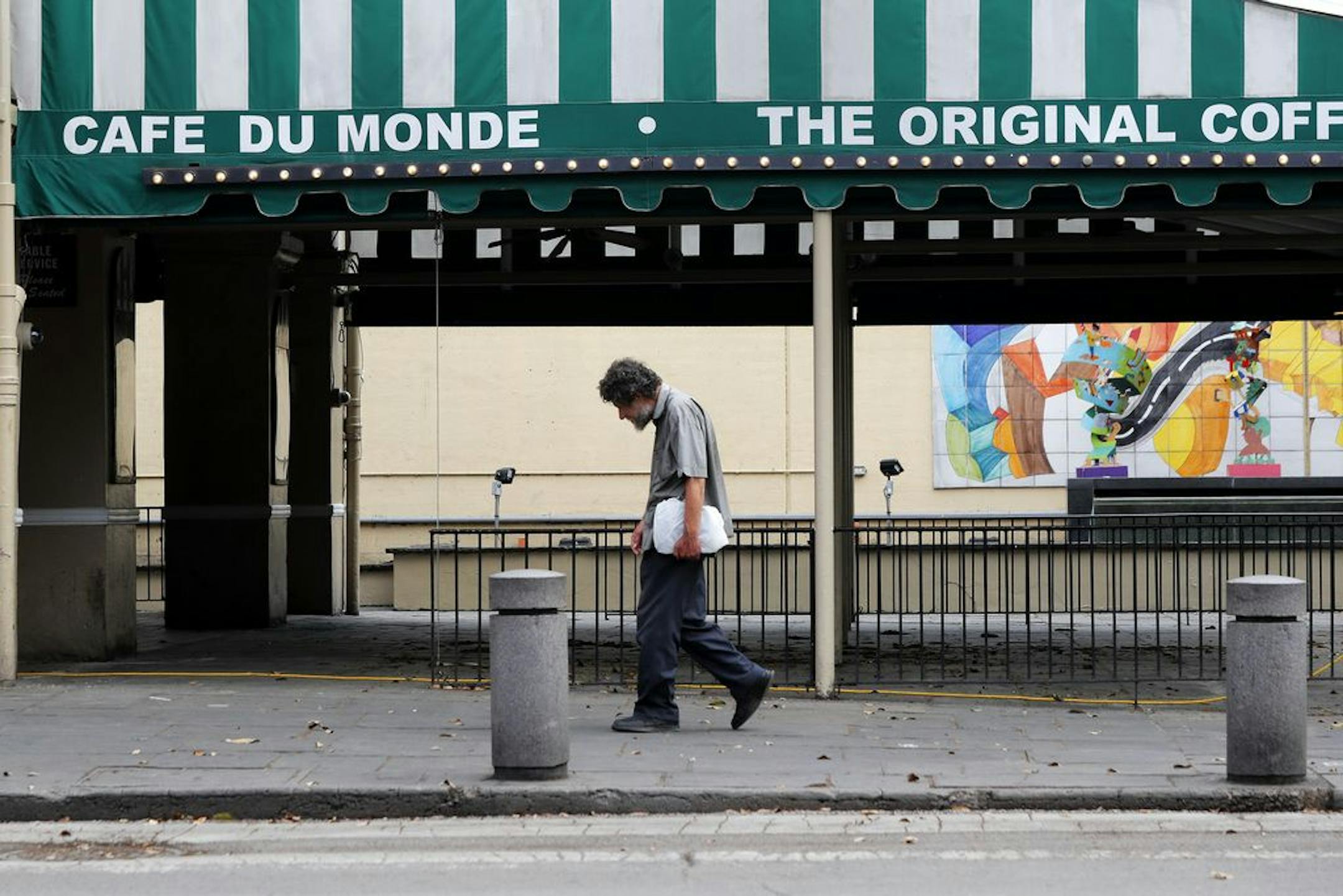 FILE - In this Friday, March 27, 2020, file photo, a man walks past the closed Cafe Du Monde restaurant in the French Quarter of New Orleans. President-elect Joe Biden will inherit a mangled U.S. economy, one that never fully healed from the coronavirus and could suffer again as new infections are climbing. The once robust recovery has shown signs of gasping after federal aid lapsed. Ten million remain jobless and more layoffs are becoming permanent. The Federal Reserve found that factory output