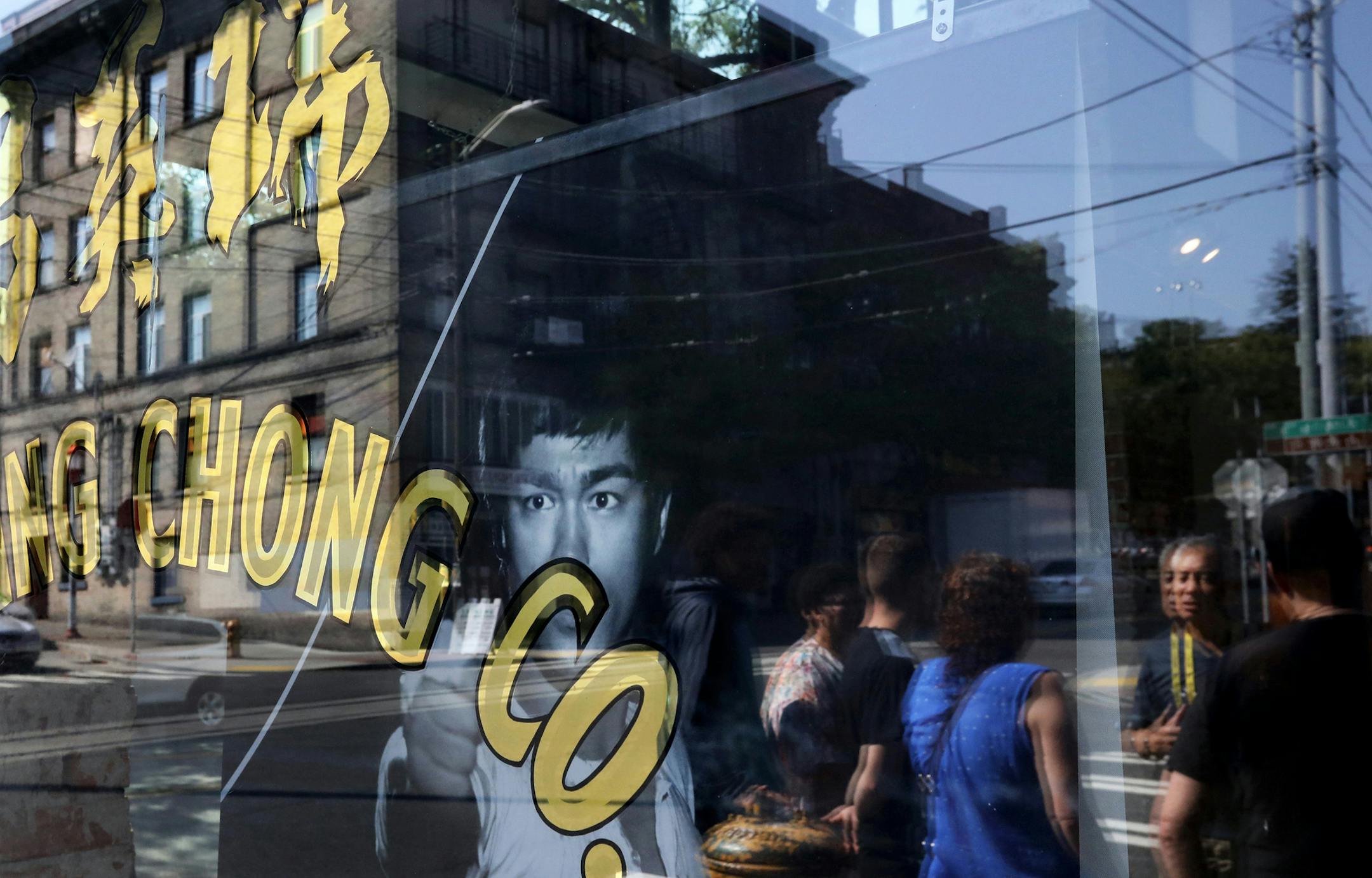 Bruce Lee looks out a window of the Wing Luke Museum as Don Wong leading a tour about the martial arts and film star is reflected, right, and the building where Bruce Lee had his second martial arts studio, reflected left. (Alan Berner/The Seattle Times/TNS)