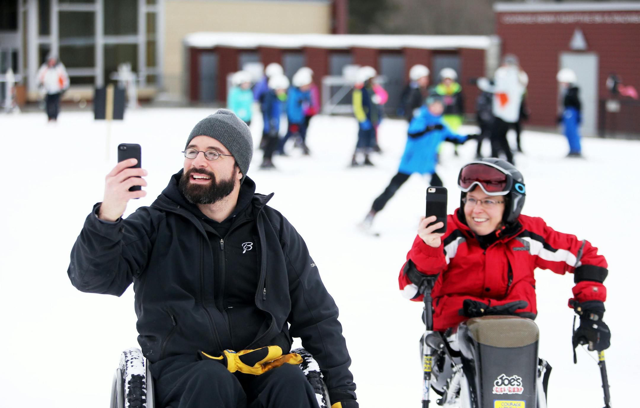 As their son Alex, 2, skis down the bunny hill with instructor Mike Knutson for the first times parents Sam, left, and Tracy Tabaka whip out cell phones to document the occasion at Hyland Hills Tuesday, Feb. 16, 2016, in Bloomington, MN.](DAVID JOLES/STARTRIBUNE)djoles@startribune.com My Outdoor Life feature on the Tabaka family, specifically Sam and Tracy, who coordinate and teach adapted sports in Three Rivers Parks District. Tracy was hurt in a car accident as a young girl and Sam in a three