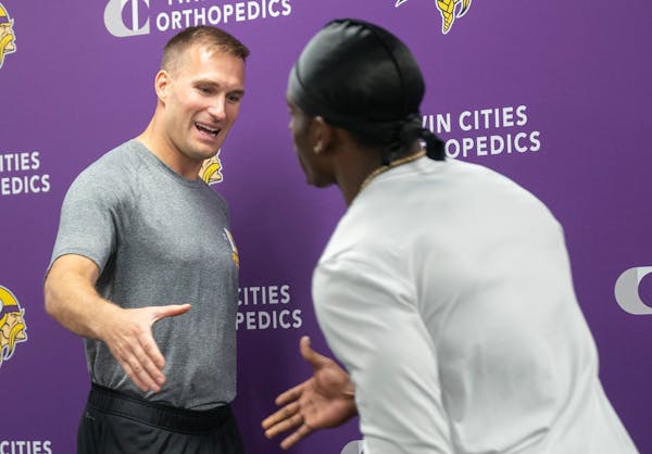 Minnesota Vikings quarterback Kirk Cousins greets cornerback Andrew Booth Jr. as they switch off speaking during a press conference.