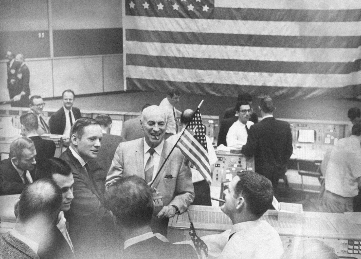 A big flag hangs in Mission Control at Manned Spacecraft Center in Houston, Tex., Dec. 27, 1968 after the completion of Apollo 8 spaceflight. Dr. Robert R. Gilruth, director of MSC holds a small flag while Astronaut Neil A. Armstrong, left, commander of Apollo 8 backup crew, congratulates Glynn S. Lunney, (white shirt) flight controller. Others are unidentified. (AP Photo) ORG XMIT: APHS362130 ORG XMIT: MIN1310071143022486