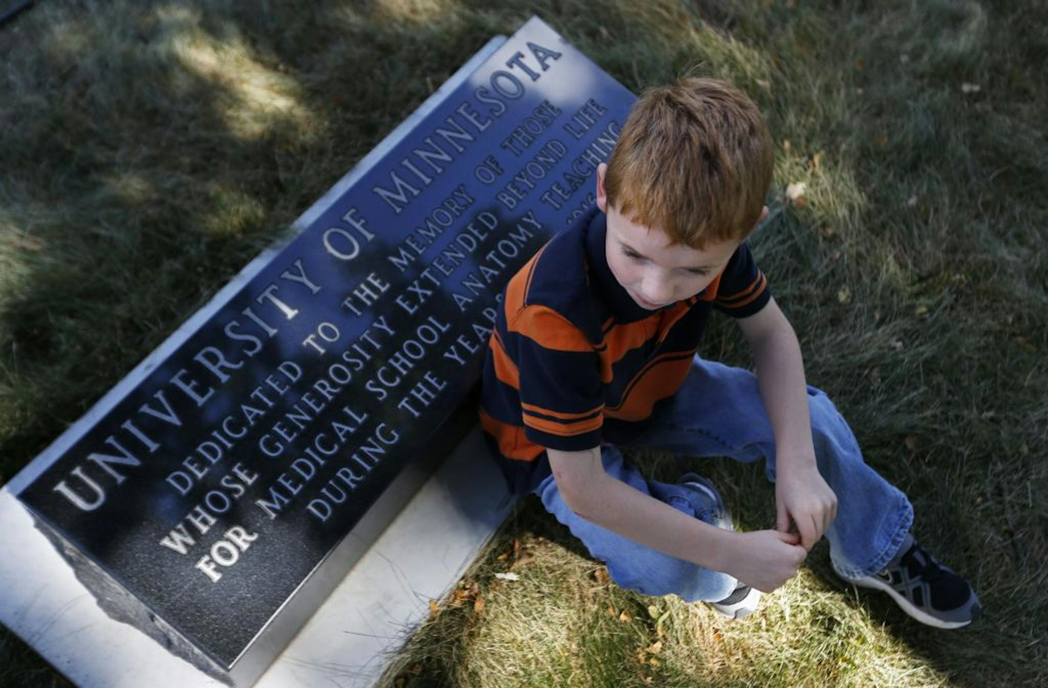 Mitch Spack,6, sits near the marker dedicated on Sunday by the University of Minnesota to honor the 350 people buried at the Pioneers and Soldiers Memorial Cemetery in Minneapolis from 1914 to 1916 whose bodies were used for medical research. Spack has a relative buried in another section of the cemetery.
